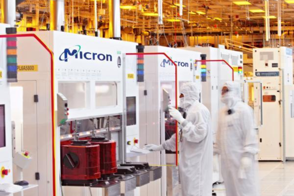 Two technicians in full cleanroom suits working on Micron semiconductor manufacturing machines